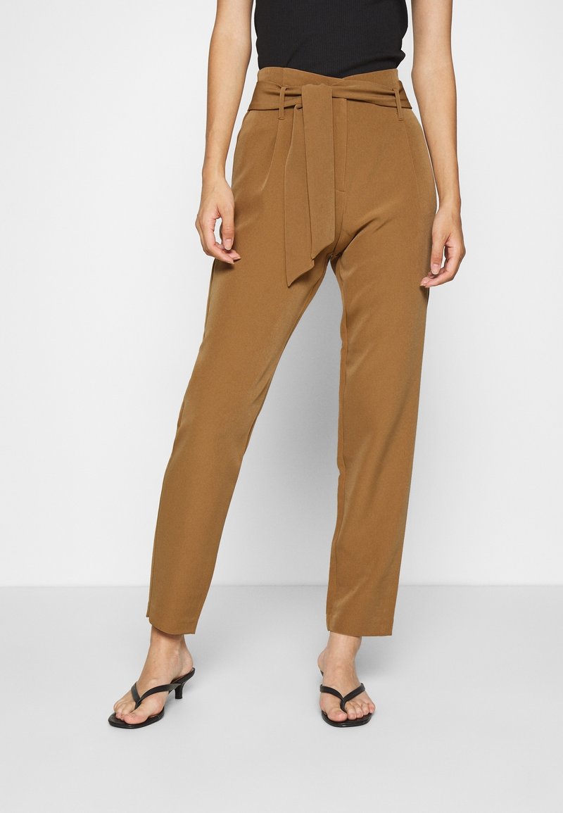 Pantalones marrones de cintura alta con detalle de cinturón atado y piernas rectas. Tela suave y diseño ajustado. Combinados con sandalias negras.