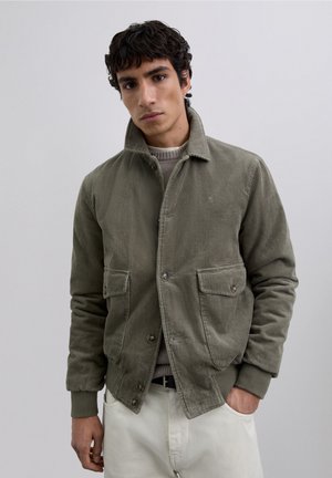 Chaqueta de pana en verde olivo, con cuello, dos bolsillos frontales, cierre de botones y puños y cintura acanalados. Textura suave.