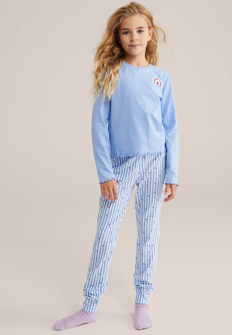 Top azul claro de manga larga con un gráfico de arcoíris, combinado con pantalones a rayas azules y blancas que presentan pequeños patrones de corazones rojos.