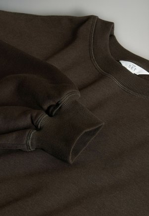 Ruskea poolopaita, jossa on ribattu hihansuu ja kaula-aukko. Pehmeä rakenne ja siistit saumat, sisäkauluksessa oleva etiketti.