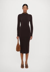 Robe midi en maille marron avec des manches longues, un col montant et une coupe près du corps. Associée à un sac marron et des chaussures à enfiler.