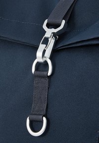 Granatowa torba z tkaniny o teksturowanej powierzchni; posiada srebrny metalowy klips i mocowanie w kształcie pierścienia, a także czarny regulowany pasek.