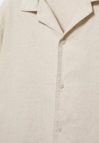 Beżowa lniana koszula z kołnierzykiem z wycięciem i trzema widocznymi okrągłymi guzikami na przedniej listwie.