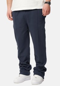 Navyblaue Jogginghosen aus weichem Stoff, mit lockerer Passform, elastischem Bund und Seitentaschen, kombiniert mit weißen Sneakern.