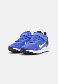 Par de zapatillas deportivas azules con swooshes de Nike en verde neón y rosa, suelas negras y tiras de Velcro sobre fondo blanco liso.