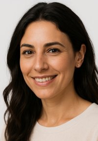 Porträt einer Frau mit langen, dunklen Haaren, die kleine metallische Ohrringe trägt. Sie hat ein warmes Lächeln und ist in einem hellen, neutralen Pullover gekleidet.