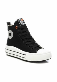 Zapatillas altas negras con parte superior de lona, puntera de goma blanca, suela estratificada y rayas contrastantes en blanco y negro. Incluye una etiqueta con el logo.