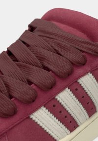 Μπούργκουντι αθλητικό παπούτσι με επίπεδους υφαντούς κορδόνια, επάνω μέρος από σουέντ και τρεις λευκές δερμάτινες ρίγες. Διαθέτει επενδεδυμένη γλώσσα και υφή λαστιχένια σόλα.