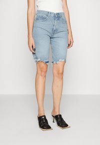 Shorts en denim bleu clair avec un ourlet effiloché, cinq poches et une coupe légèrement ample, associés à des mules à talons noirs avec un bout carré.