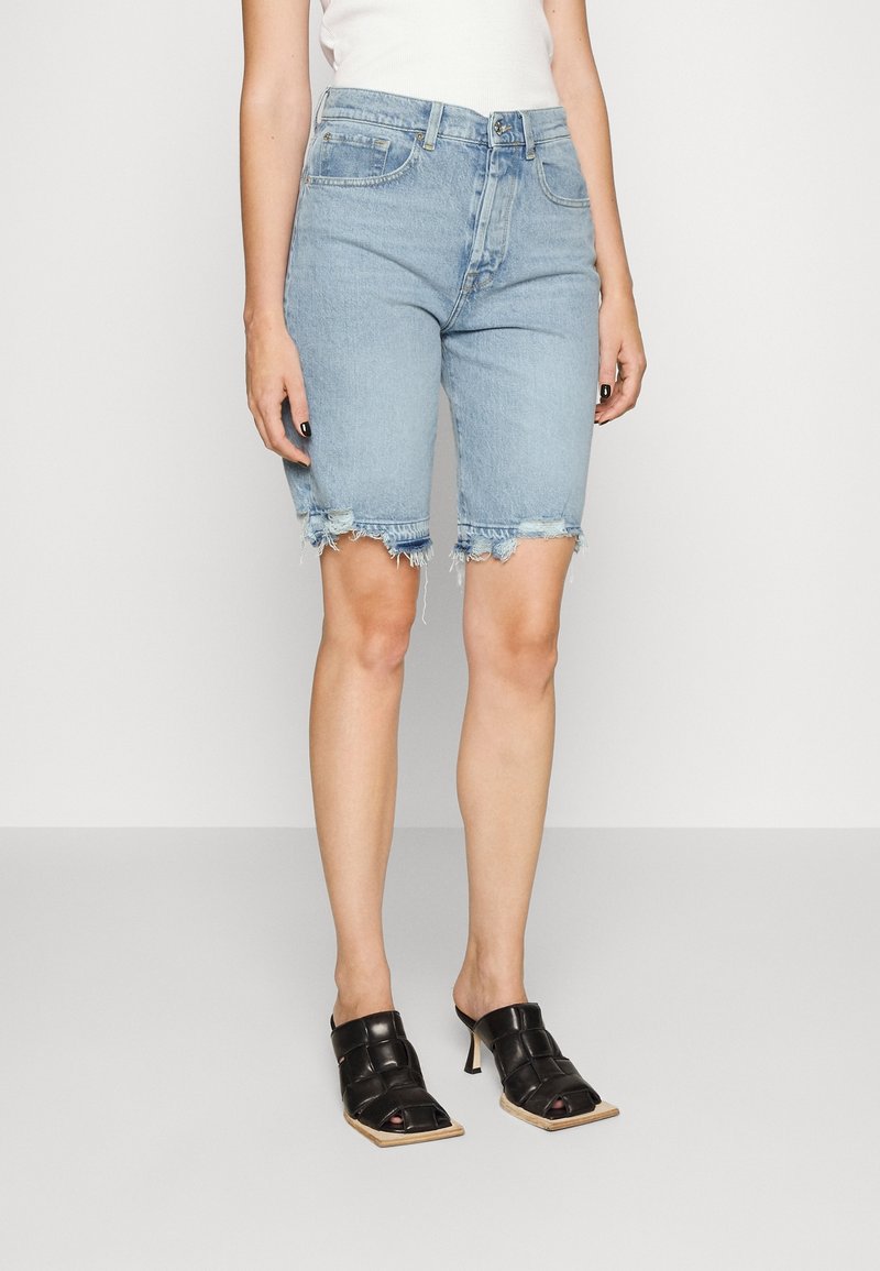 Shorts en denim bleu clair avec un ourlet effiloché, cinq poches et une coupe légèrement ample, associés à des mules à talons noirs avec un bout carré.