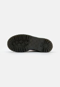 Suela de zapato de goma negra con profundas ranuras, que presenta una superficie texturizada y patrones de tracción para agarre y estabilidad.
