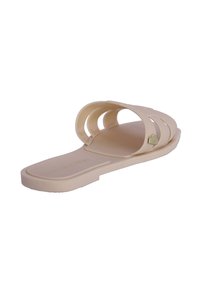 Chancla de goma beige con tres correas anchas y curvas, y un pequeño acento en forma de corazón. Textura suave, suela plana y diseño abierto.