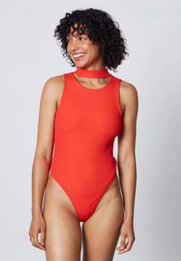 Body rosso a coste con collo alto, design senza maniche e dettagli cut-out aperti sul collo, con uno stile gambale alto.