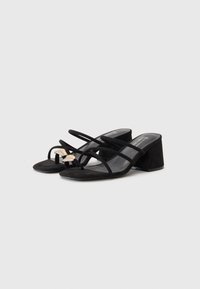 Sandalias de tacón cuadrado de ante negro con múltiples tiras finas, que presentan un acento dorado en la parte delantera. Textura suave con un diseño abierto.