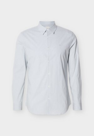 Világoskék csíkos, hosszú ujjú pamuting. Klasszikus gallér, gombos elülső rész és állítható mandzsetták jellemzik. Apró logó a mellrészen.