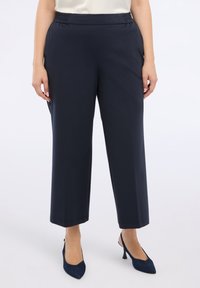 Marineblaue dehnbare Hose mit lockerer Passform, ausgestattet mit einem elastischen Bund und geradem Schnitt. Kombiniert mit spitzen marineblauen Absätzen für einen Kontrast.