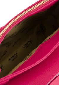 Lyserød lædertaske med tekstureret overflade og guld lynlås; beige indre med gentaget "Venezia" logo tryk.