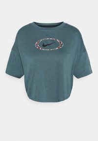 T-shirt blu cropped a maniche corte con scollatura rotonda e logo Nike ovale circondato da un motivo floreale sul petto.
