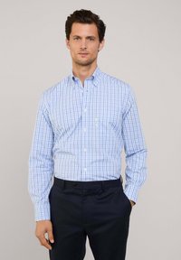 Camicia a scacchi blu chiaro e bianca con colletto button-down, maniche lunghe, taschino sul petto, abbinata a pantaloni blu navy.