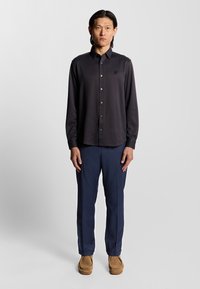 Mörkt mönstrat skjorta med krage, matchat med marinblå byxor och tan loafers. Markant textur och figurnära design.