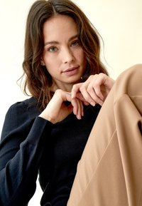 Maglione nero a maglia con maniche testurizzate abbinato a pantaloni beige a gamba larga, che mostrano una vestibilità rilassata e tonalità neutre. Sfondo chiaro.