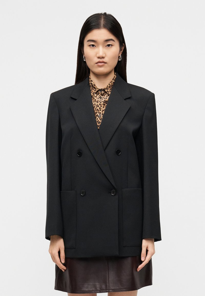 Μαύρο διπλό σακάκι με μεγάλα πέτα, δύο εμπρόσθιες τσέπες και λεπτομέρειες με κουμπιά. Φορεμένο πάνω από πουκάμισο με λεοπάρ σχέδιο.