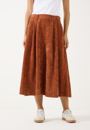 Woman wearing a rust-colored, ribbed corduroy midi skirt with belt loops paired with white sneakers and a white top.