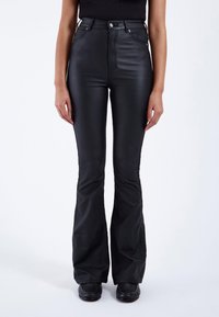 Hoge taille zwarte flared broek van glanzend materiaal, met een ritssluiting aan de voorkant, twee zakken en een aansluitend ontwerp op de bovenbenen.