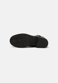 Semelle d'une chaussure de ville noire avec un motif antidérapant texturé et un petit talon, présentée sur un fond clair uni.