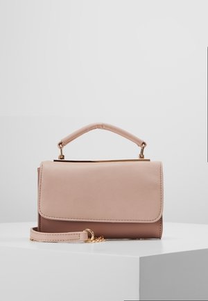 Mała prostokątna torebka w kolorach beżowym i brązowym z górnym uchwytem i odpinanym paskiem na nadgarstek na białym postumencie.