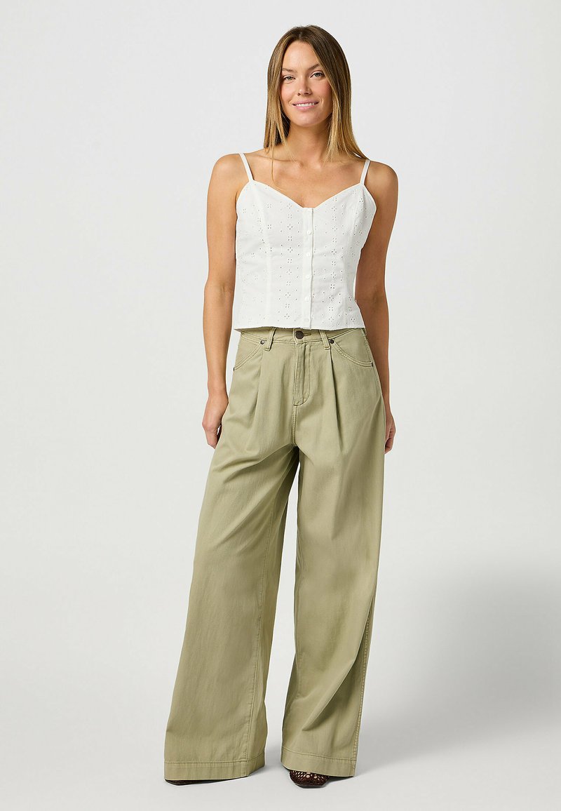 Haut court blanc avec des détails en œillets et des boutons ; pantalon large vert olive ; tissu naturel, coupe décontractée et surface texturée.