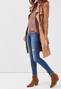 Brown suede trench coat over a patterned orange and blue blouse, paired with distressed blue skinny jeans and brown ankle boots with a block heel.