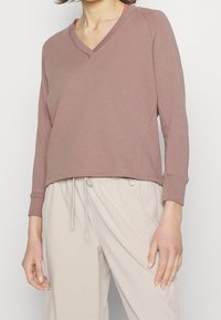 Felpa rosa polveroso con scollo a V in morbido cotone misto. Presenta maniche lunghe e un fit rilassato, abbinata a pantaloni beige chiaro con cordino.