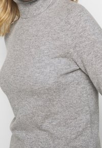 Light gray turtleneck sweater made of soft knit fabric. Features a fitted design with ribbed collar and smooth texture.