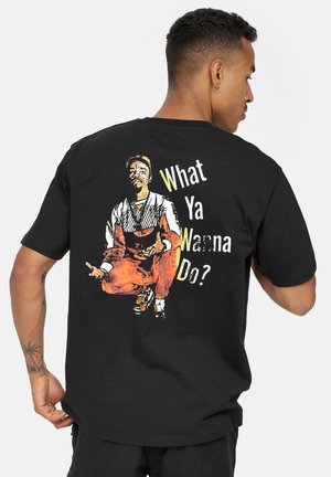 T-shirt nera in cotone con stampa grafica sulla parte posteriore di una figura seduta con la scritta "Cosa vuoi fare?" in bianco e giallo.