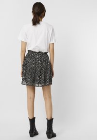Gonna nera a fiori con design plissettato, caratterizzata da vita alta e vita arricciata, abbinata a una t-shirt bianca semplice e stivali neri alla caviglia.
