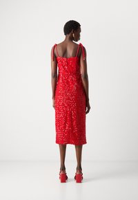 Robe midi rouge avec une silhouette ajustée, ornée de sequins, avec de fines bretelles réglables et un ourlet droit. Les chaussures sont des sandales à talons blocs rouges.