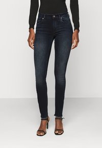 Donkere blauwe skinny jeans van denim met een subtiel vervaagd patroon. Heeft een taille op middenhoogte, voorzakken en een onafgewerkte zoom.