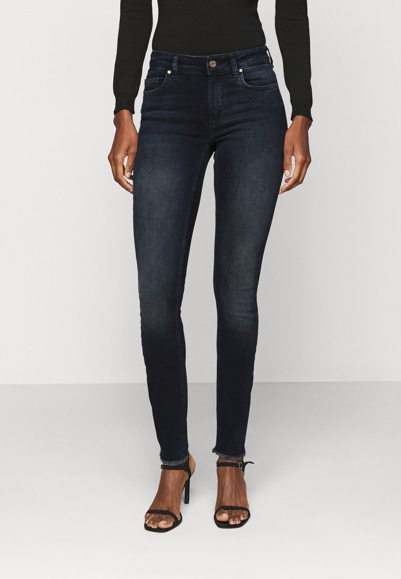 Donkere blauwe skinny jeans van denim met een subtiel vervaagd patroon. Heeft een taille op middenhoogte, voorzakken en een onafgewerkte zoom.