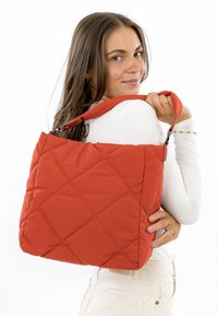 Quilted orange shoulder bag made of padded fabric, featuring a square pattern and a sturdy strap attached to a metallic clasp.