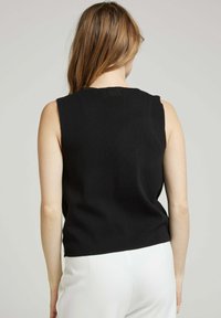 Haut sans manches noir avec une texture côtelée, présentant un col haut et un design ajusté, associé à un pantalon de couleur claire.