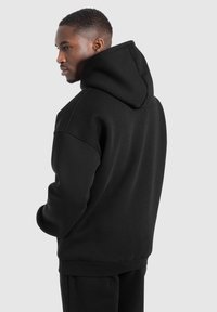 Felpa nera con cappuccio realizzata in tessuto morbido, caratterizzata da un ampio cappuccio, polsini e orlo a coste. Vestibilità casual e rilassata con una texture liscia.