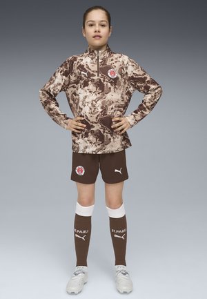 Braunes Camouflage-Sporttrikot mit halbem Reißverschluss und Logo, kombiniert mit braunen Shorts und knielangen Socken, die weiße Akzente und Markenkennzeichnung aufweisen.