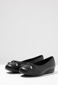 Svarta läderballerinor med rund tå, knuten rosett och silverdetaljer på rosetten, med en slät yta och låg klack.