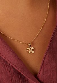 Goldene Halskette mit einem bogenförmigen Anhänger und einem kleinen Edelstein in der Mitte. Die Kette ist fein und zart und liegt sanft auf der Haut.