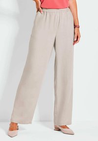Helle beige weite Hosen mit elastischem Bund, ausgestattet mit einer glatten Textur und seitlichen Taschen, kombiniert mit weichen, spitzen beigen Schuhen.