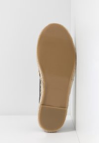 Chaussure noire avec une semelle en caoutchouc texturé de couleur sable et un accent en jute tissé. Semelle plate et design à bout rond. Détails simples et minimalistes.