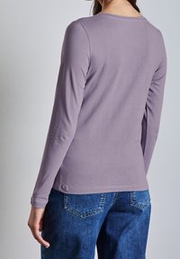 Långärmad skjorta i ljuslila tyg med rundad halsringning, slät textur och smal passform, ihop med blå denimjeans.