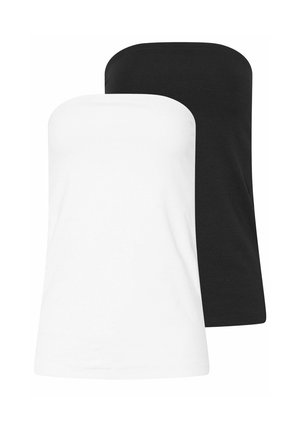 Femme aux longs cheveux blonds portant un haut blanc sans bretelles, un jean bleu et des baskets blanches, debout devant un fond beige.