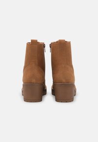 Bottines en daim marron avec un talon épais, une texture lisse et des fermetures éclair latérales dissimulées. Détails de coutures le long des coutures.